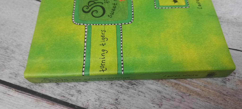 A close-up of a green and yellow painted canvas print featuring the text 'turning tigers' and decorative stitched borders, resting on a light-colored wooden surface.