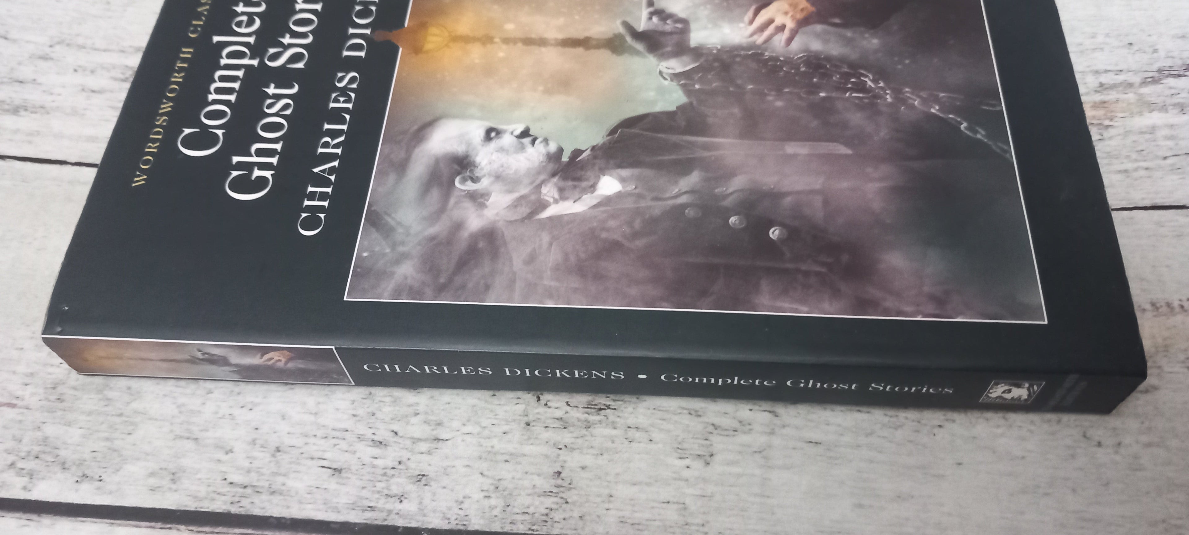 The book 'The Complete Ghost Story' by Charles Dickens, featuring a black cover with a dark, moody illustration and white title text, resting on a light-colored wooden surface.
